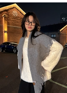 Detail of grey knitted winter scarf with long tassels shown in an outdoor street setting