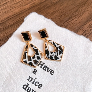 Détail de boucles d'oreilles géométriques dorées avec texture résine marbrée noire et blanche