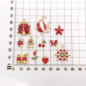 Dettagli macro di ciondoli in smalto rosso e oro su griglia graduata per gioielli DIY