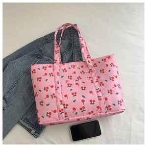 Detailed view of a pink tote bag with cherry patterns on a soft white fabric background