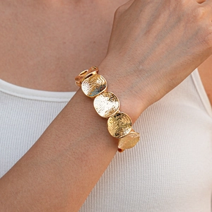 Dettaglio di un ampio bracciale dorato con dischi metallici rotondi martellati e testurizzati