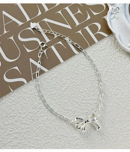 Detail of silver S925 bowknot chain bracelet with heart charm on a textured background