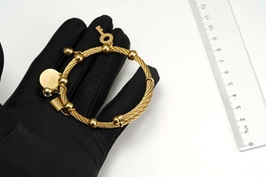 Close-up of gold braided cable bracelet with key and lock charms shown with a ruler