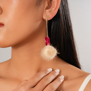 Close-up of golden snowflake stud earrings with red bow and beige fur ball pendants
