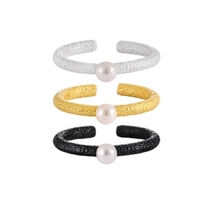 Three textured cuff bracelets in silver, gold, and black with central pearls on white backdrop