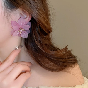 Close-up of pink petal flower earrings with pearls worn by a model in soft lighting
