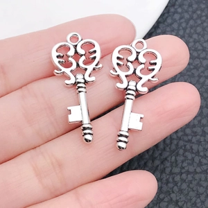 Close-up of vintage silver key charms held on a finger to show the precise product scale