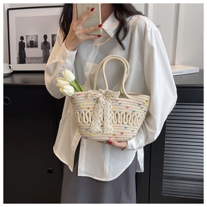 Detail of cream woven bucket bag featuring colorful pom-poms and a lace bow decoration