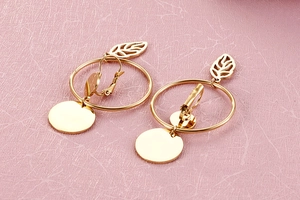 Detailed view of gold hoop earrings with leaf charms on pink textured background
