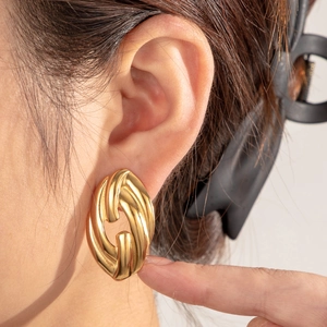 Golden twisted oval hoop earrings in stainless steel worn by a model in a high-quality shot