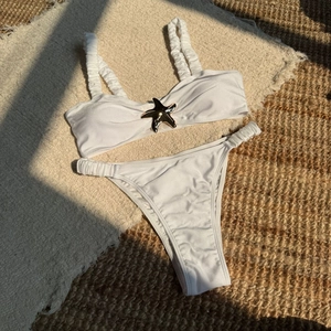 Flat lay of white bikini with textured fabric and starfish metal detail on beach rug