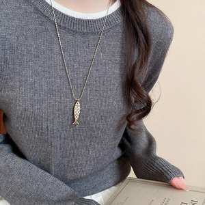 Close-up of a golden fish pendant with white enamel detail on a model wearing a sweater