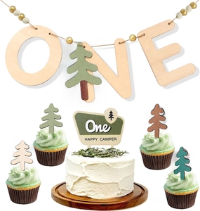 Close-up of wooden One Happy Camper cake topper and pine tree decorations for birthday party
