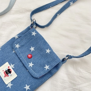 Detailopname van blauwe denim crossbodytas met sterrenpatroon en rode knopversiering
