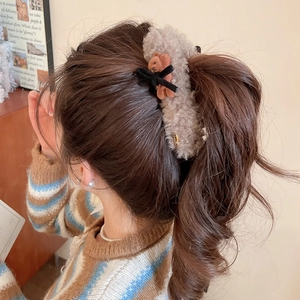 Detail view of a plush brown bear hair clip with a black bow worn on a ponytail hair
