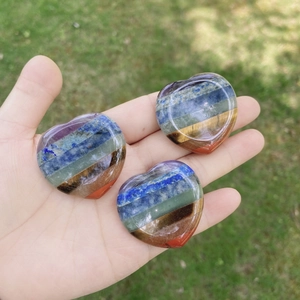 Polished heart-shaped chakra stones with seven-color layers held over a green lawn