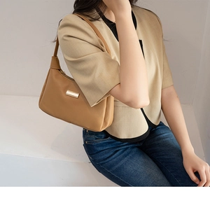 Detail of caramel brown hobo shoulder bag with lychee texture and gold metal plaque
