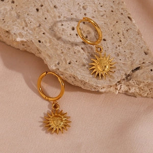 Detailed shot of golden sun face charm earrings on a textured mineral stone background