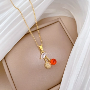 Elegant gold cherry necklace with red beads and marquise crystal on beige jewelry box