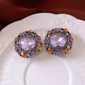 Macro shot of vintage style earrings with purple crystals on a white ceramic plate