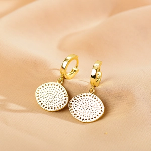 Macro detail of gold round geometric drop earrings on soft pink silk background