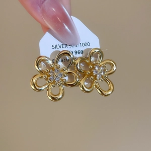 Close-up of golden flower stud earrings with zircon inlay on a white jewelry card