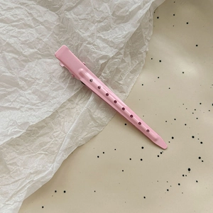 Detailed view of long pink metal hair clip with circular hollow design on beige surface