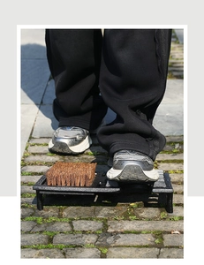 Detail of vintage cast iron boot scraper with stiff brown bristles on stone path