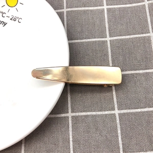 Detail view of a minimalist golden hollow duckbill hair clip on a checkered fabric background
