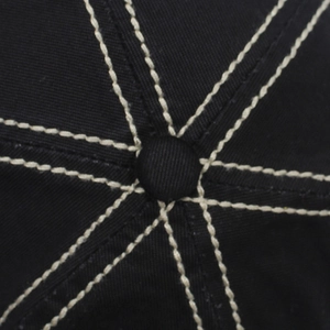 Macro detail of black cotton baseball cap crown with white contrast stitching and top button