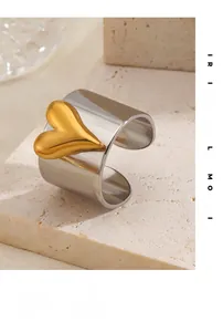 Gros plan d'une bague large argentée avec cœur doré sur une pierre beige texturée