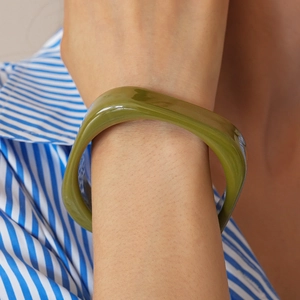 Detail showing an olive green thick resin bangle on a model wrist for fashion style