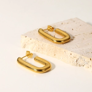 Close-up of polished 18K gold-plated U-shaped earrings on a natural stone tray