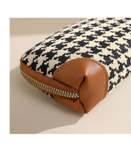Macro detail of houndstock fabric with tan leather trim and golden zipper on hand clutch