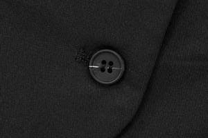 Detailed close-up of a black resin button on textured diamond quilted waistcoat fabric