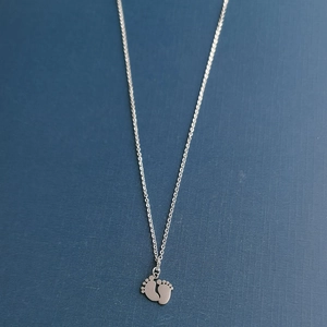 Polished stainless steel necklace with silver baby footprint pendant on blue background