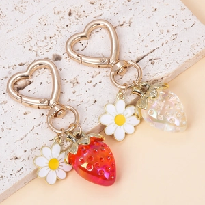 Close-up of strawberry keychains with heart hooks and flowers on a textured stone