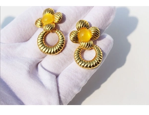 Détail macro de boucles d'oreilles florales dorées vintage avec perle en résine jaune