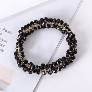 Detailed view of black faceted beaded hair tie woven on a beige cord over an open book