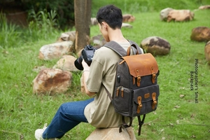 Photographer wearing a grey canvas camera backpack with leather trim in an outdoor setting