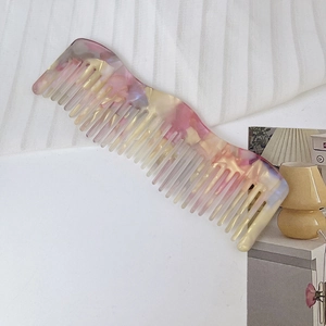 Macro shot of wavy acetate hair comb featuring pastel marble texture and wide teeth