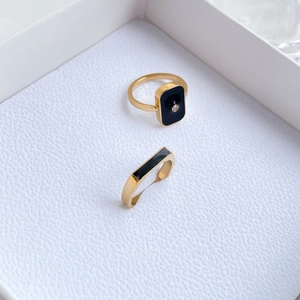 Close-up of golden square rings with black enamel inlay and diamond detail in a jewelry box
