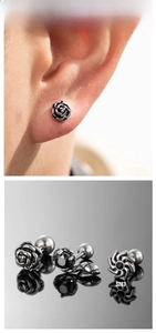 Detail of punk style stainless steel stud earrings featuring rose, snake, and sun motifs