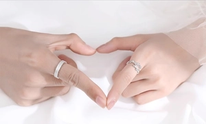 Close-up of vine-textured silver rings worn by hands forming a heart shape
