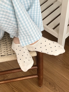 Détail de chaussettes beiges en coton à pois noirs portées sur un sol en bois clair