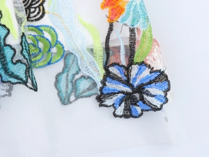 Dettaglio macro del ricamo floreale 3D colorato sul tessuto a rete velata dell'abito