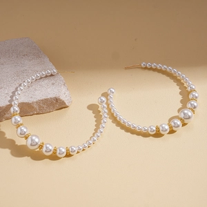 Detail of C-shaped hoop earrings featuring gradient pearls and gold beads on stone