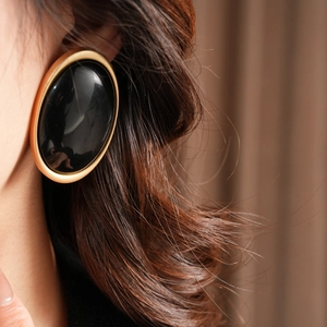 Close-up of vintage oval resin earrings with matte gold frame and glossy black stone inlay