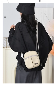 Detail of a beige nylon crossbody bag with front zipper pockets worn by a model