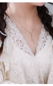 Detail of a gold S925 silver Y-shaped necklace with cross and gem on a female neck